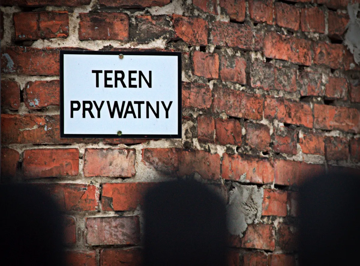Private property sign mounted on a red brick wall behind blurred dark fence bars